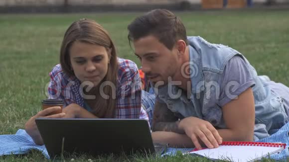 两个学生在草坪上用笔记本电脑讨论一些事情视频的预览图
