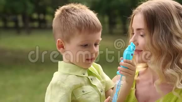 微笑的年轻母亲和小儿子一起在公园里吹泡泡肥皂视频的预览图
