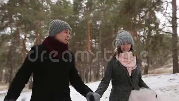 户外冬季拍摄年轻的新婚夫妇在雪天松林中奔跑玩得开心视频的预览图