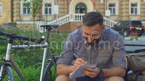Cyclist在长凳上的笔记本上写字视频的预览图