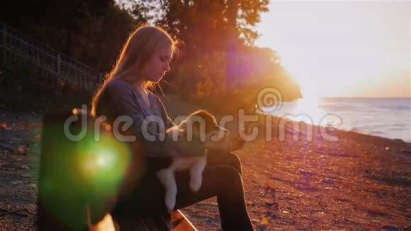 年轻女子在湖边或海边的公园里读电子书日落时分坐在长凳上抱在怀里视频的预览图