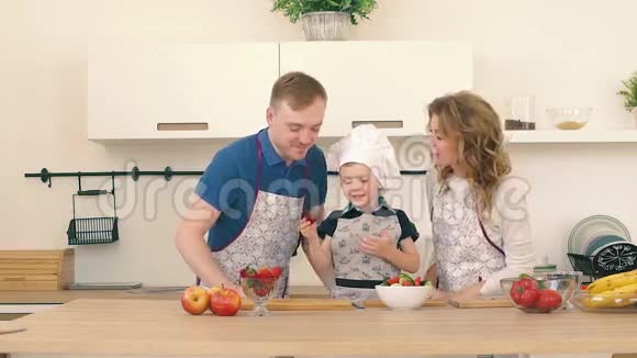父母正在亲吻他们的儿子一个孩子在厨房为爸爸妈妈准备水果沙拉视频的预览图