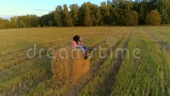 母亲带着女儿坐在夕阳下的田园上的草垛上视频的预览图