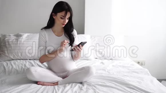 带手机的孕妇在卧室的床上视频的预览图