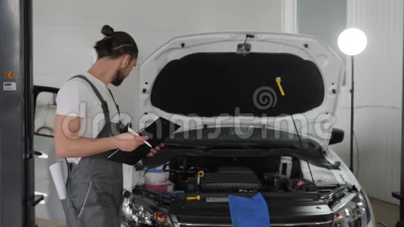 专业机械师站在打开引擎盖的车旁边向女性客户解释引擎盖下的问题视频的预览图