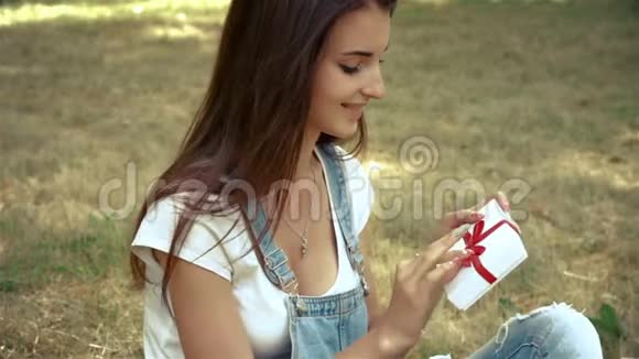 夏天美丽的女人坐在公园的草坪上微笑并保留礼物视频的预览图