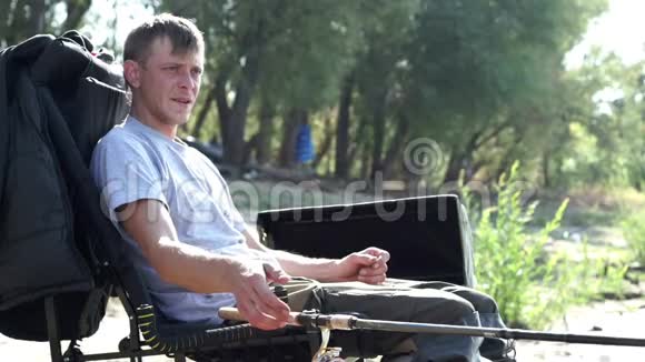 年轻的渔夫坐在河边的椅子上几乎是鱼竿等待着咬人视频的预览图