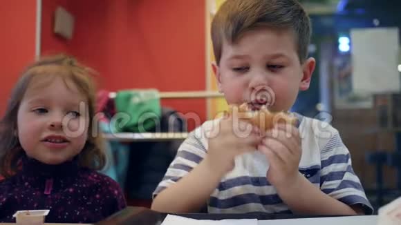 孩子们边吃边说话男孩子咀嚼汉堡包有趣的孩子在快餐店里玩食物美味的薯条视频的预览图
