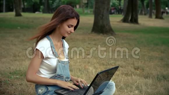 可爱的小女孩双腿手提电脑坐在草坪上视频的预览图