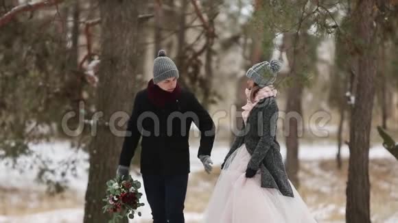 户外冬季拍摄年轻的新婚夫妇在雪天松林中奔跑玩得开心视频的预览图