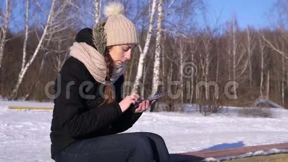 冬季森林晴天智能手机上的妇女浏览图片文字号码视频的预览图
