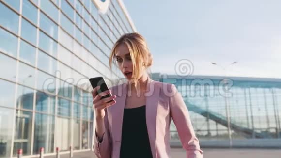 漂亮的年轻女子急急忙忙地走到商务中心用她的电话得到消息惊讶跳跃视频的预览图