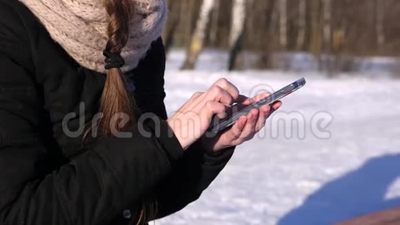 冬季晴天智能手机上的妇女浏览图片文字号码视频的预览图