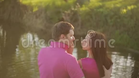日落时分一个漂亮的女孩和一个男人坐在河边在户外约会的情侣视频的预览图