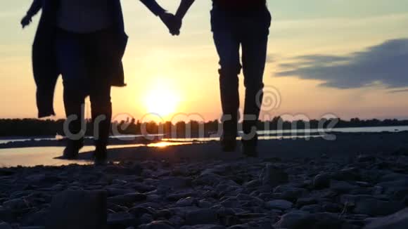 一对相爱的夫妇牵着手在日落的背景下沿着石滩奔跑高清1920x1080慢动作视频的预览图