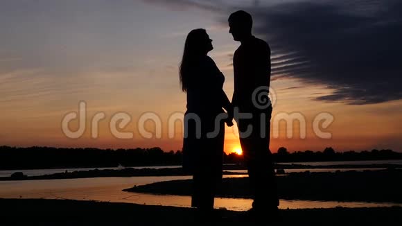 女孩和男朋友亲吻在美丽的夕阳和河流的背景下高清1920x1080慢动作视频的预览图