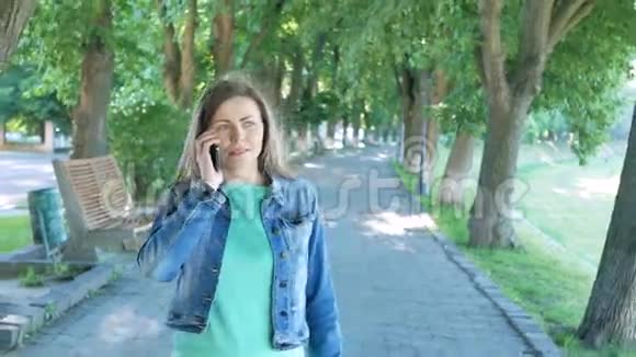 年轻女子在智能手机上漫步公园车道在公园散步的漂亮女孩视频的预览图