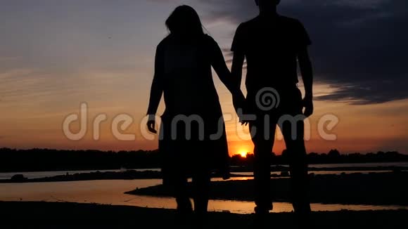 一对相爱的夫妇在日落时牵着手在河边散步高清1920x1080慢动作视频的预览图