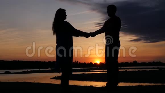小伙子和姑娘牵着手迎着美丽的夕阳和小河高清1920x1080慢动作视频的预览图