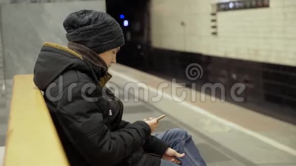 那家伙坐在地铁的长凳上把脚放在腿上一个穿着冬装的少年坐在长椅上视频的预览图
