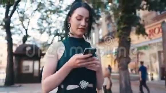 可爱的年轻女孩使用她的智能手机而走在城市的街道上抚摸她的头发短信回来微笑存在于视频的预览图