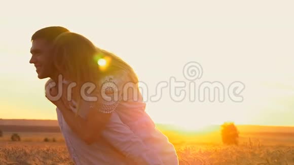 年轻漂亮的一对女孩和男孩在日落时在麦田里嬉戏和调情他把女孩抱在身上视频的预览图