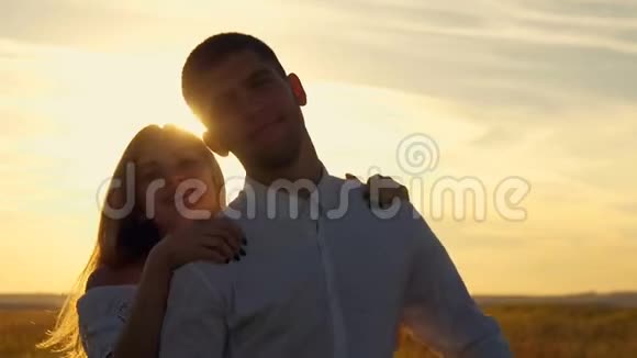 年轻漂亮的一对女孩和男孩在日落时在麦田里嬉戏和调情他把女孩抱在身上视频的预览图