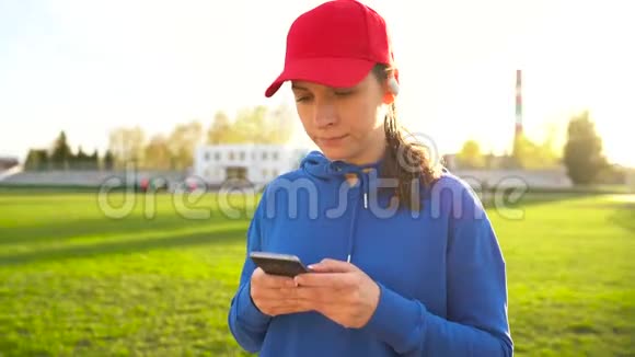 拥有无线耳机和智能手机的女士选择音乐日落时分穿过体育场视频的预览图