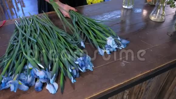 花商妇女创造花束从蓝色虹膜花在桌子上出售在商店视频的预览图