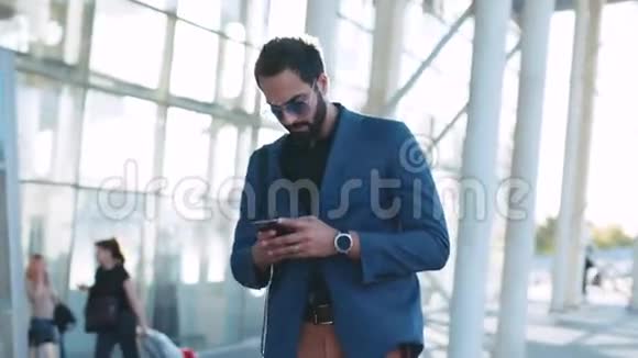 一个穿着休闲服的漂亮男人经过机场候机楼用他的电话欣然地回答了收到的视频的预览图