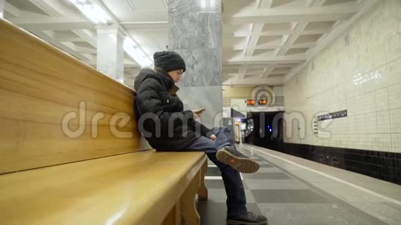 那家伙坐在地铁的长凳上把脚放在腿上一个穿着冬装的少年坐在长椅上视频的预览图