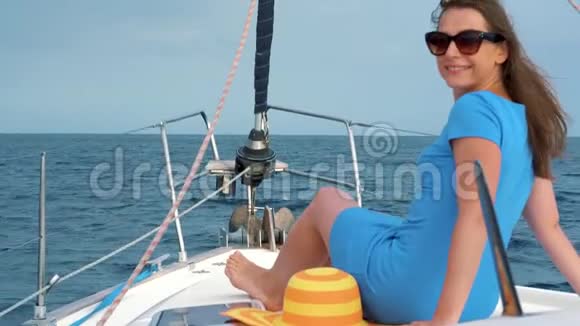 穿着黄色帽子和蓝色连衣裙的女人在海洋的夏天在游艇上挥舞着头发和微笑慢动作视频的预览图