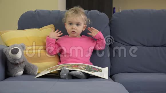 两岁可爱的女婴坐在沙发上看故事书展示情感视频的预览图