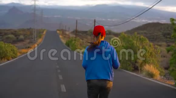 日落时分女人沿着荒芜的沥青路奔跑后景背景上的山脉慢动作视频的预览图