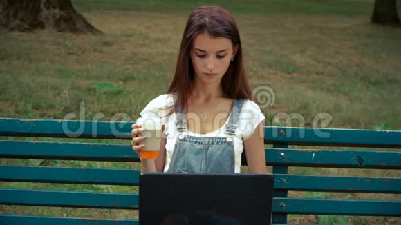 年轻迷人的黑发女人喝咖啡盯着笔记本电脑视频的预览图