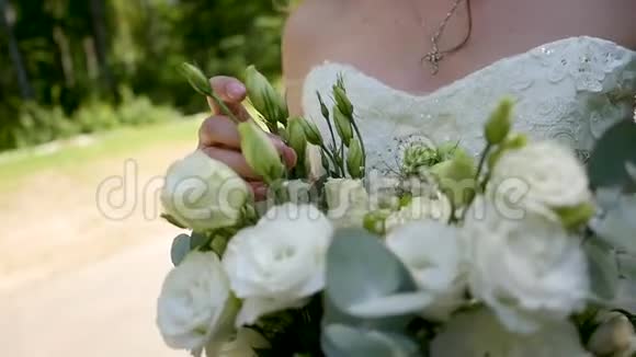 美丽的年轻新娘穿着婚纱在阳光明媚的公园里开着花视频的预览图