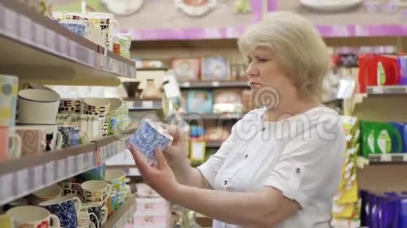 老年妇女在超市选择彩色陶瓷杯在商店里购物高级女性仔细分析视频的预览图