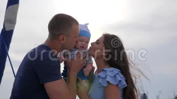 家庭在阳光下的肖像父母为婴儿亲吻心情好的年轻夫妇与儿子在露天视频的预览图