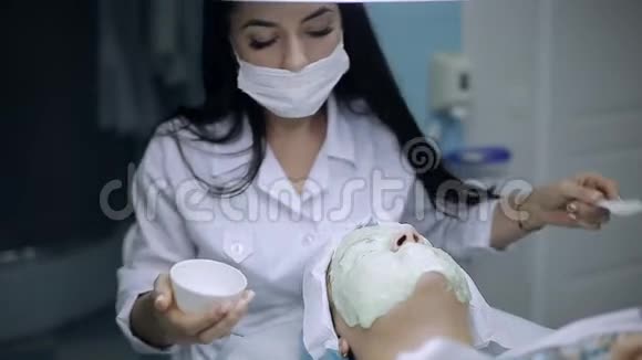 美容师在一个皮肤有问题的年轻女孩的脸上涂上一层面膜视频的预览图