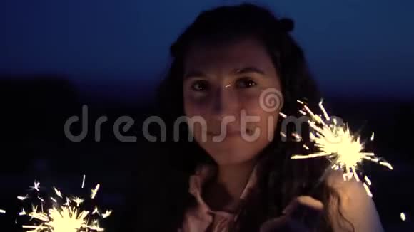 一个留着长发的年轻女孩站在一个夜晚城市的背景下手里拿着烟花慢动作视频的预览图