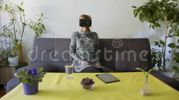 家里的女人在沙发上享受虚拟现实护目镜视频的预览图
