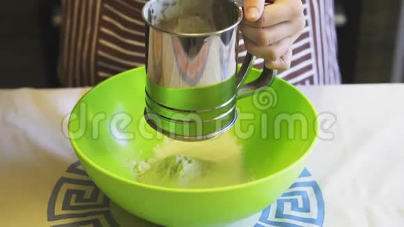 在家中的厨房里用一个绿色的碗里的筛子杯子特写一只雌性手筛面粉烹饪煎饼视频的预览图