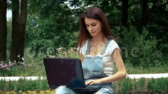 女孩把笔记本电脑的指纹放在街道上的花坛附近视频的预览图