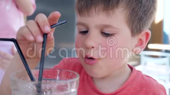 男孩在舒适的街头咖啡馆里坐在桌上用玻璃吸管喝饮料美丽的孩子做零食视频的预览图