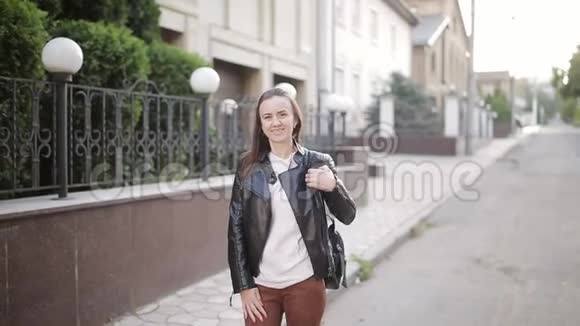一个穿着皮夹克和背包的女孩站在街上的肖像他的新家的背景视频的预览图