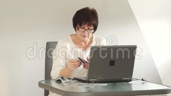 一位老年妇女用笔记本电脑和银行卡支付账单网上付款视频的预览图