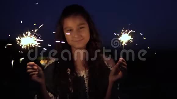 一个留着深色长发的年轻女孩晚上放着烟火很高兴慢动作视频的预览图