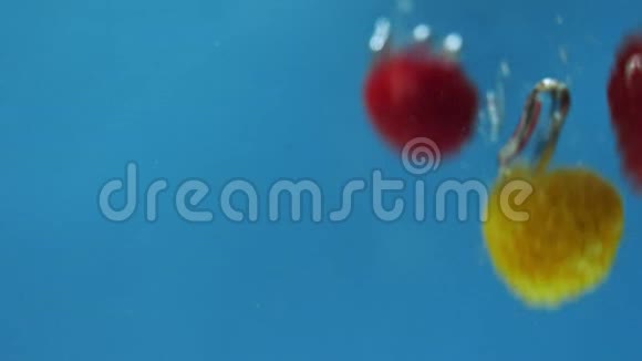 许多红色和黄色的覆盆子正在蓝色背景下掉进水里视频的预览图