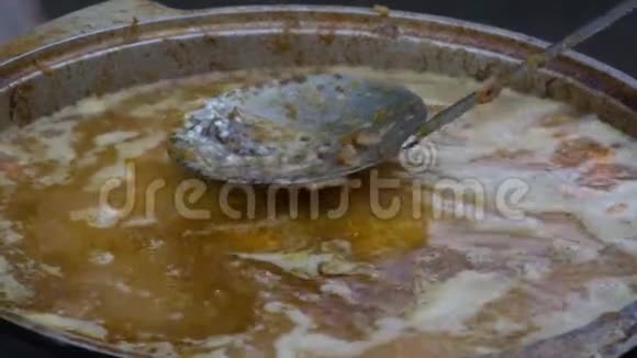 肉与米饭和蔬菜在木桩处的大锅里煮熟厨师用搅拌器搅拌原料视频的预览图