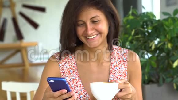 女人在智能手机上阅读信息喝咖啡开怀大笑视频的预览图